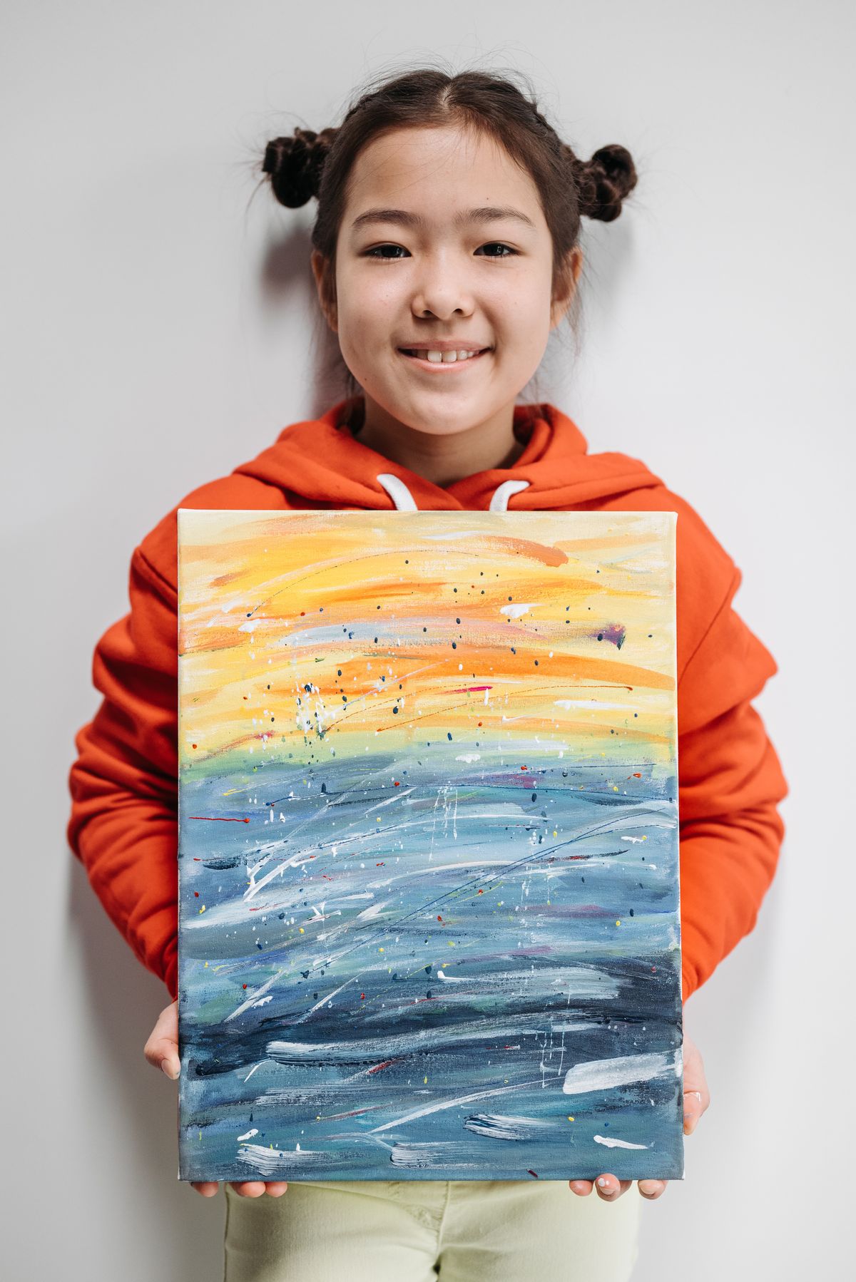Une enfant souriante présente sa peinture multicolore.