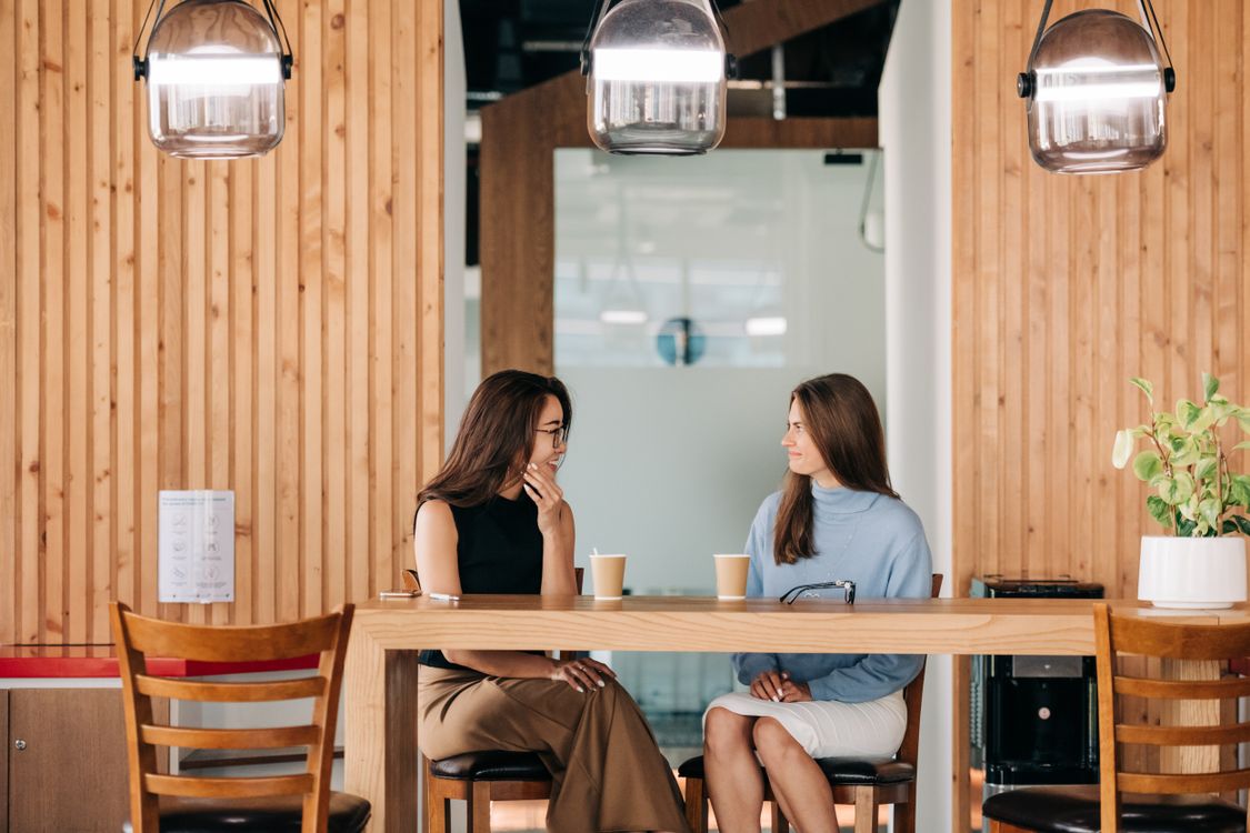 Deux femmes échangent avec le sourire autour d’un café.