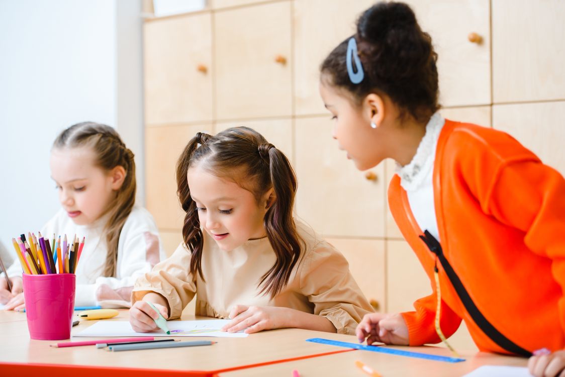 Trois enfants dessinent ensemble autour d’une table à l’école.